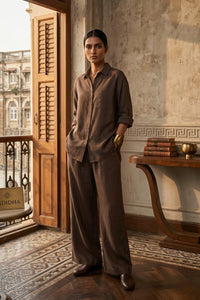 Woman in a brown outfit standing in a room with a wooden door and decorative wall.