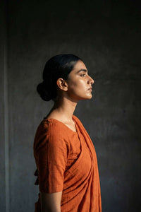 Woman in an orange saree standing against a dark background