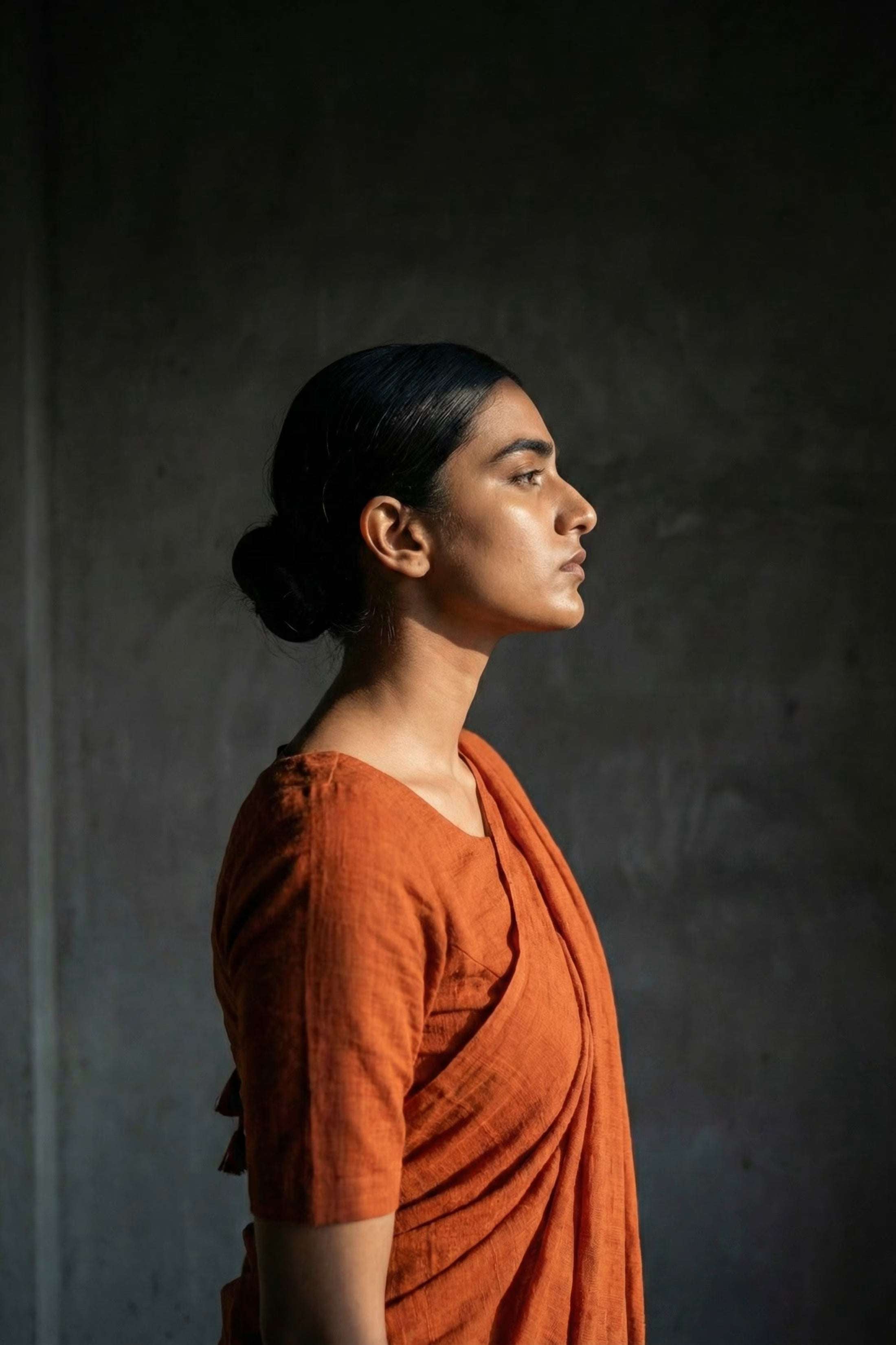 Woman in an orange saree standing against a dark background