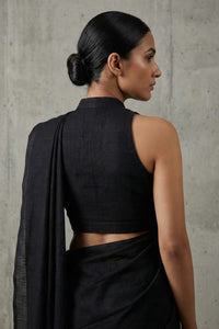 Woman wearing a black saree against a gray concrete wall