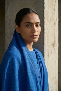 Woman wearing a blue saree standing against a neutral wall.
