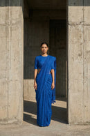 Woman in a blue saree standing between two concrete pillars.