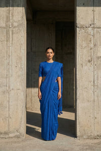 Woman in a blue saree standing between two concrete pillars.
