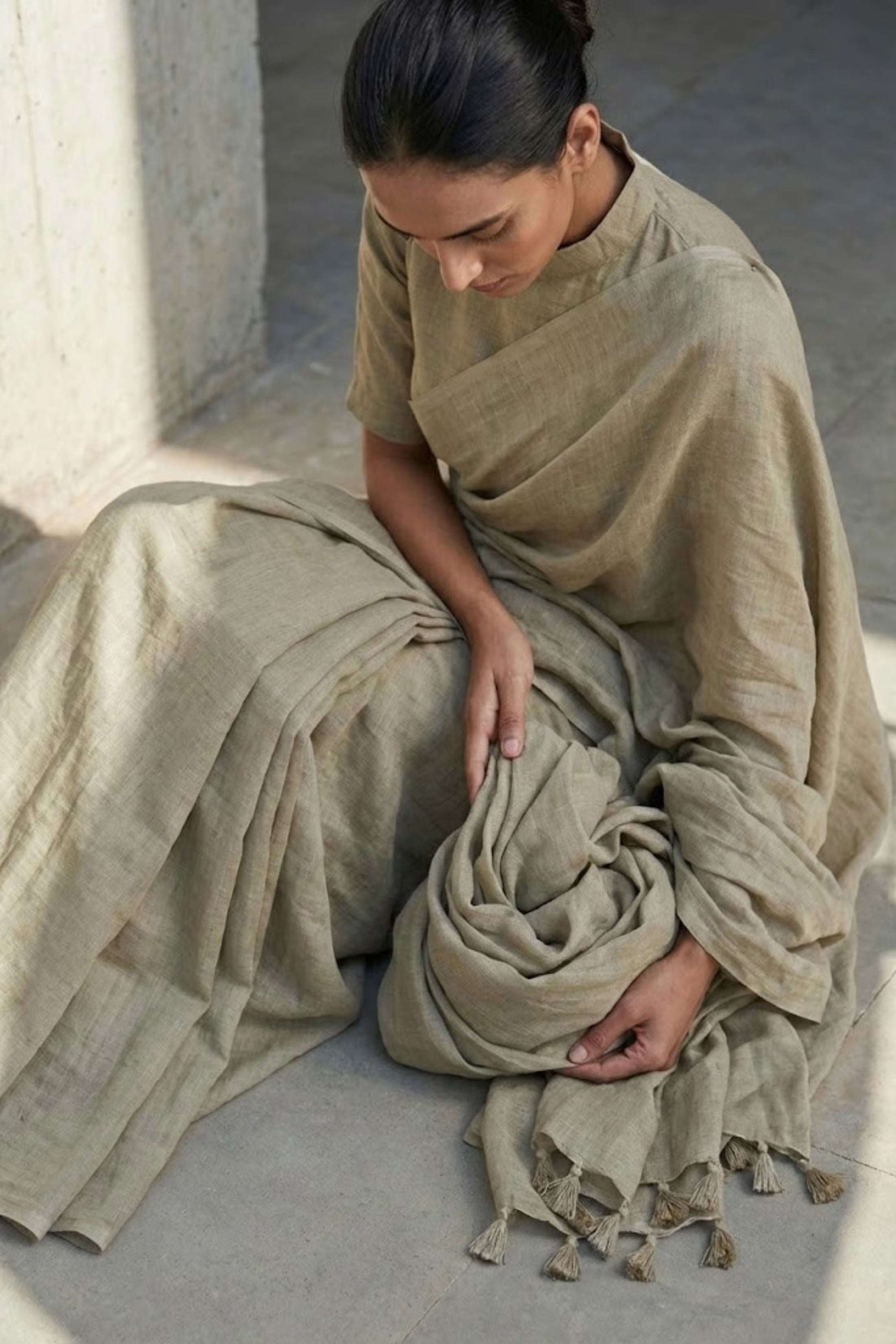 Woman sitting on a stone floor wearing a beige saree with a plain background