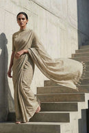 Woman in a beige saree standing on stone steps against a light-colored wall.