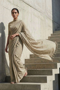 Woman in a beige saree standing on stone steps against a light-colored wall.