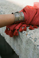 Silver bracelet with red fabric and tassels on a stone surface