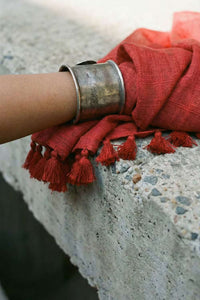 Silver bracelet with red fabric and tassels on a stone surface