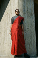 Person wearing a red saree and black blouse against a textured wall.
