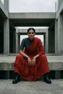 Woman in a red saree sitting on concrete steps with a modern architectural background