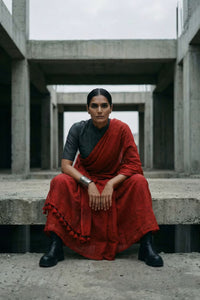 Woman in a red saree sitting on concrete steps with a modern architectural background
