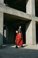 Person wearing a red saree and black blouse standing in a concrete architectural setting