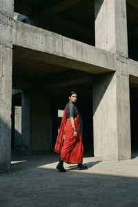 Person wearing a red saree and black blouse standing in a concrete architectural setting