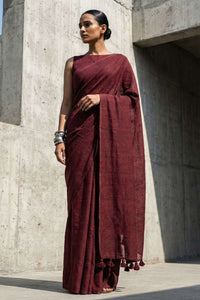 Woman in a maroon saree standing against a concrete wall.