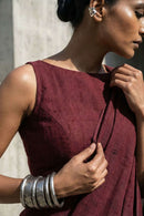 Woman wearing a burgundy sleeveless top with silver bangles, against a neutral background.