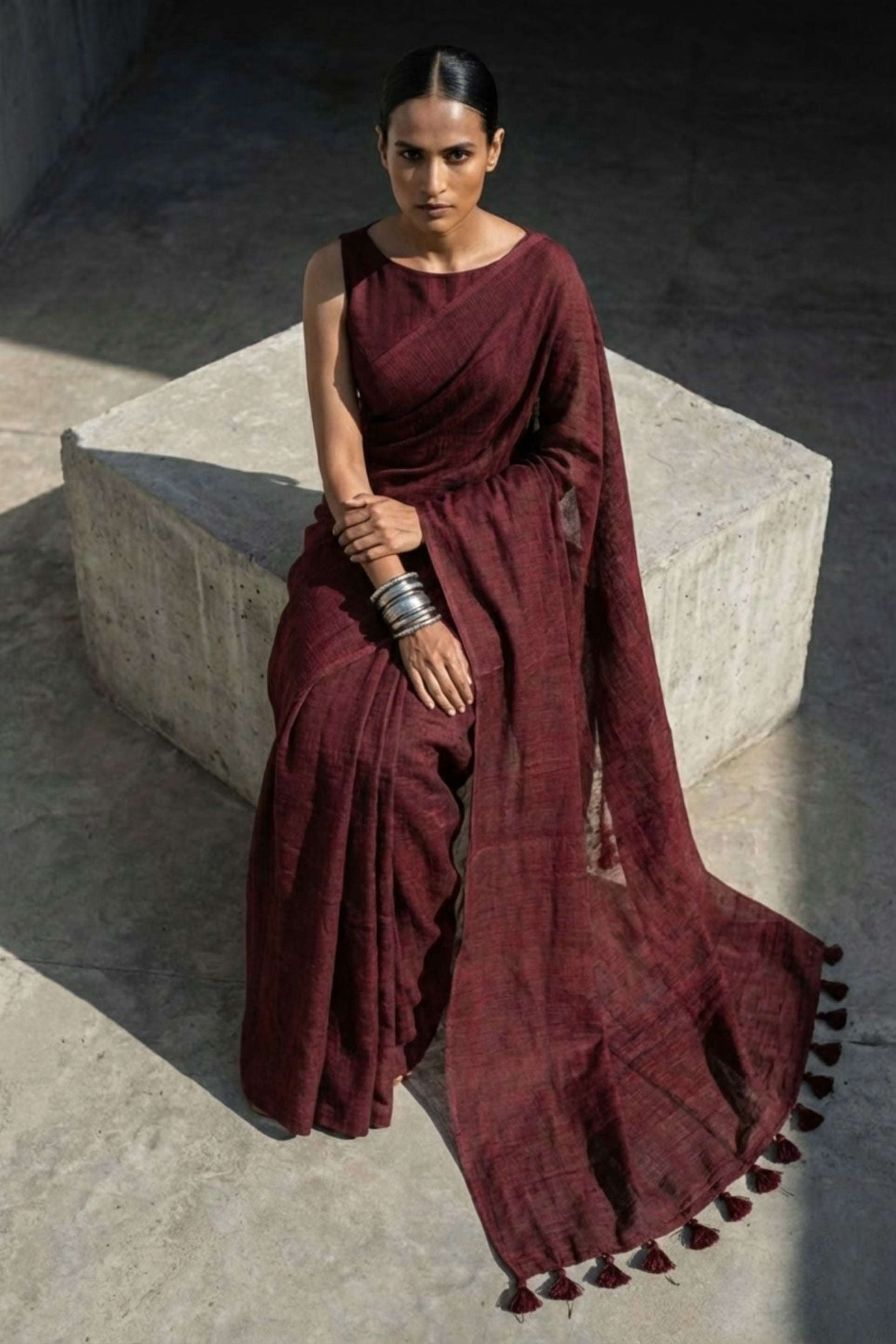 Woman in a burgundy saree sitting on a concrete bench.