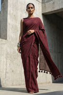 Woman in a maroon saree standing against a concrete wall.