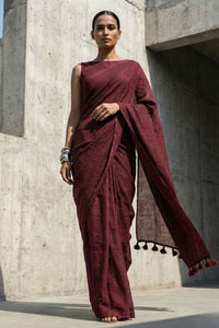 Woman in a maroon saree standing against a concrete wall.