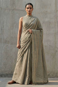 Woman wearing a beige saree against a plain wall