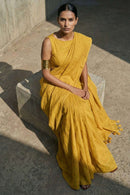 Woman in a yellow saree sitting on a stone bench outdoors.