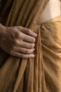 Close-up of a hand holding brown mul cotton sari.