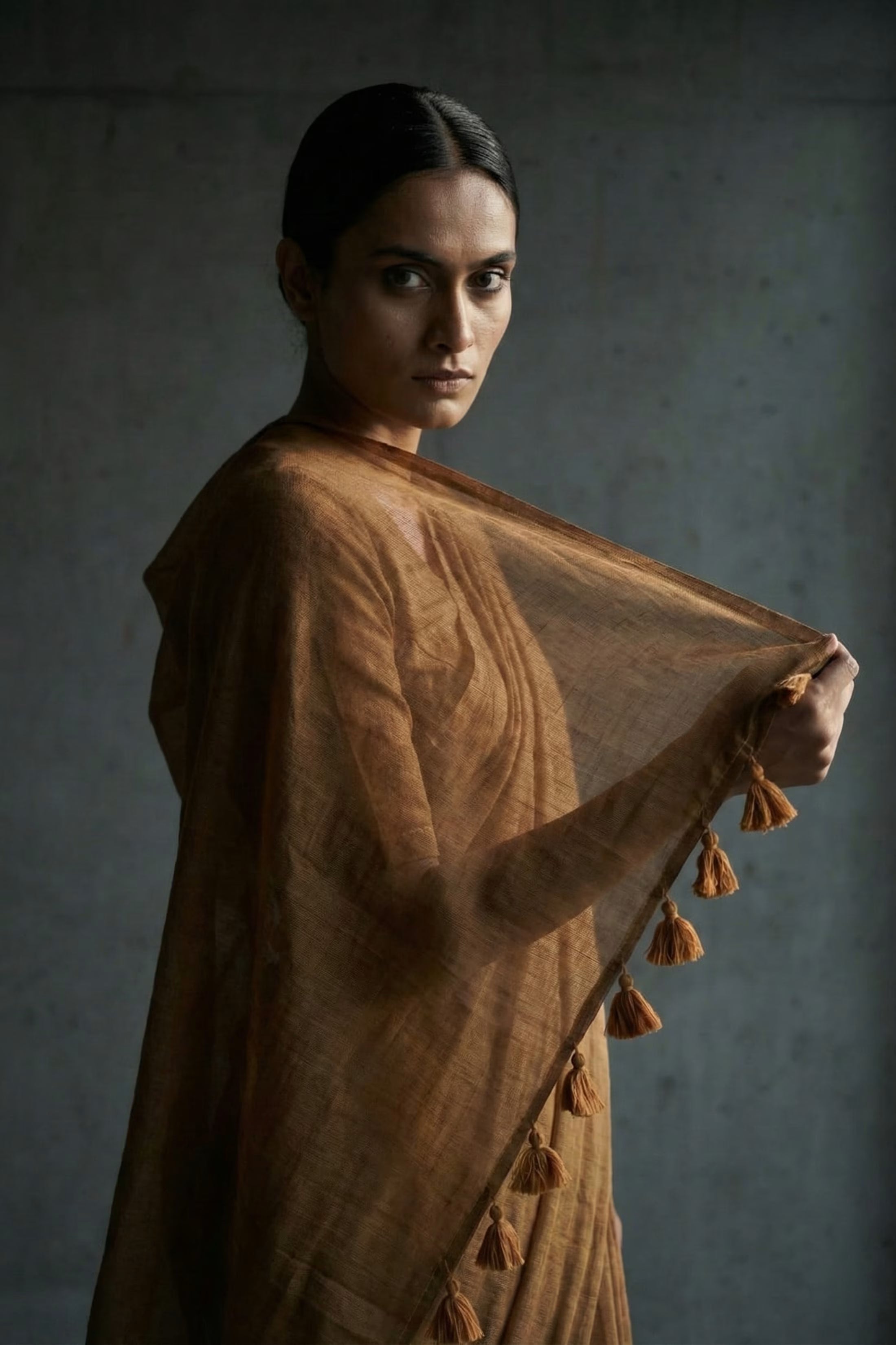 Woman holding a brown mul cotton saree with tassels against a dark background