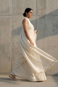 Woman in a flowing white saree against a textured wall.