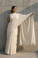 Woman wearing a white saree against a concrete wall