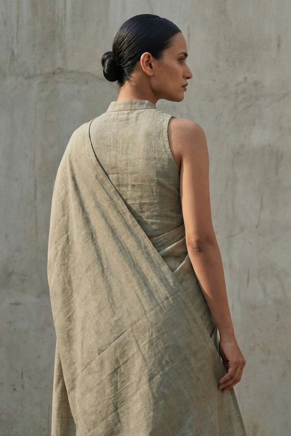 Woman wearing a beige draped saree against a plain wall