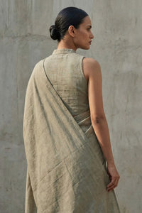 Woman wearing a beige draped saree against a plain wall