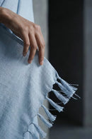 Light blue saree with tassels held by a hand against a dark background