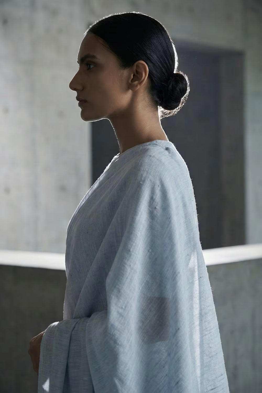 Woman in a light blue saree standing in a softly lit room.