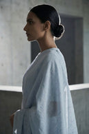 Woman in a light blue saree standing in a softly lit room.
