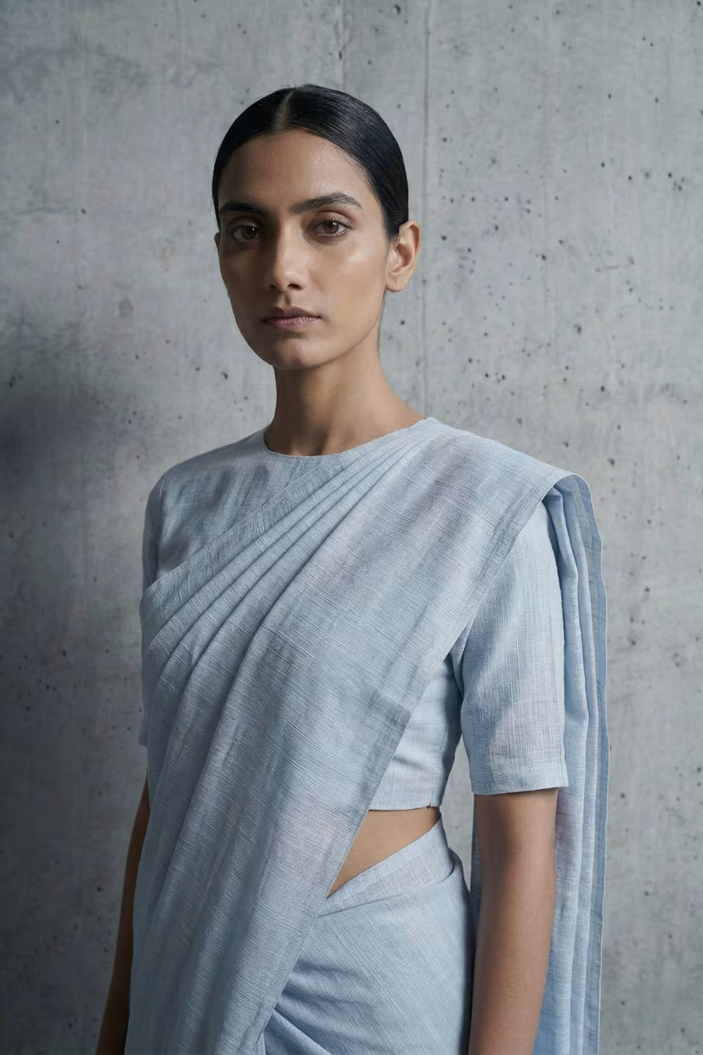Woman wearing a light blue saree against a gray concrete wall
