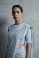 Woman wearing a light blue saree against a gray concrete wall