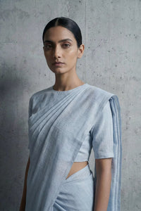 Woman wearing a light blue saree against a gray concrete wall