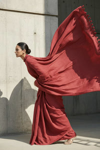 Woman in a flowing red dress against a concrete wall.