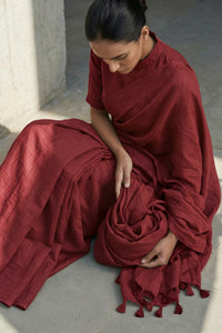 Woman in a red saree sitting on a stone floor.