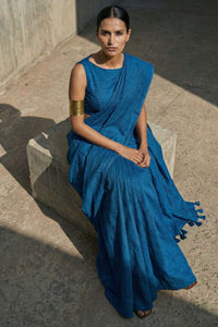 Woman in a blue saree sitting on a stone bench outdoors.