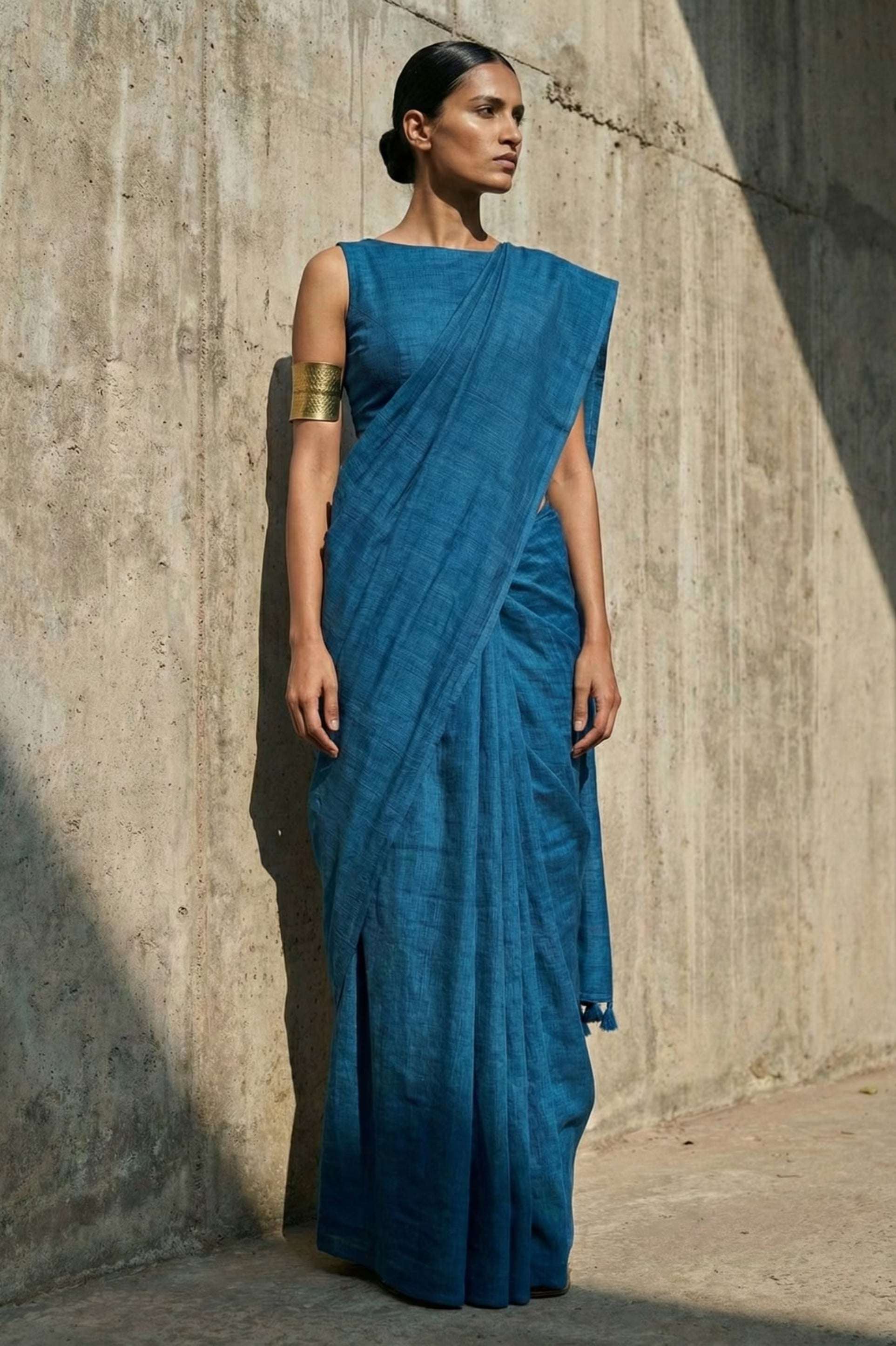 Woman wearing a blue saree standing against a textured wall.