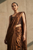 Woman wearing a brown saree against a beige wall