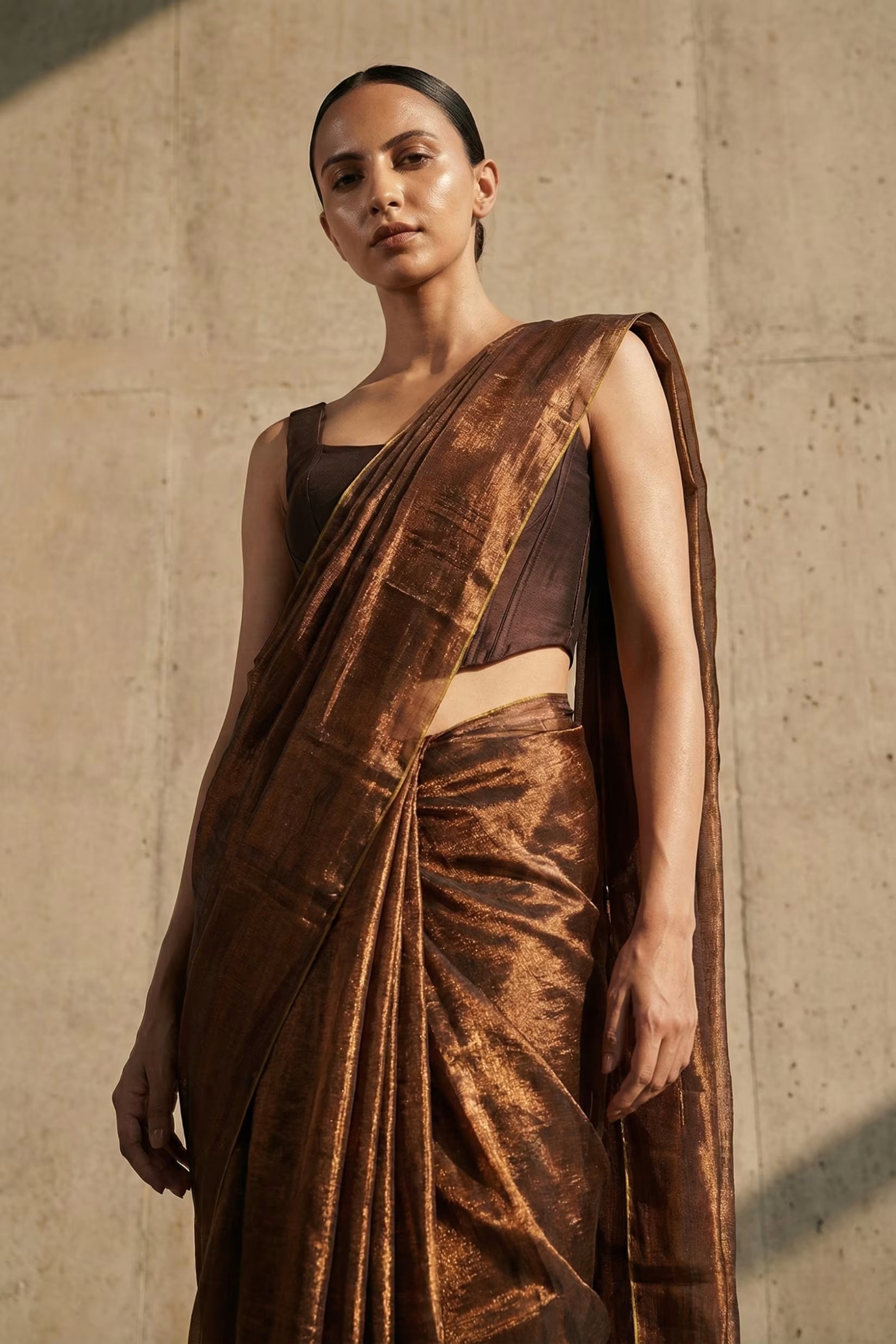 Woman wearing a brown saree against a beige wall