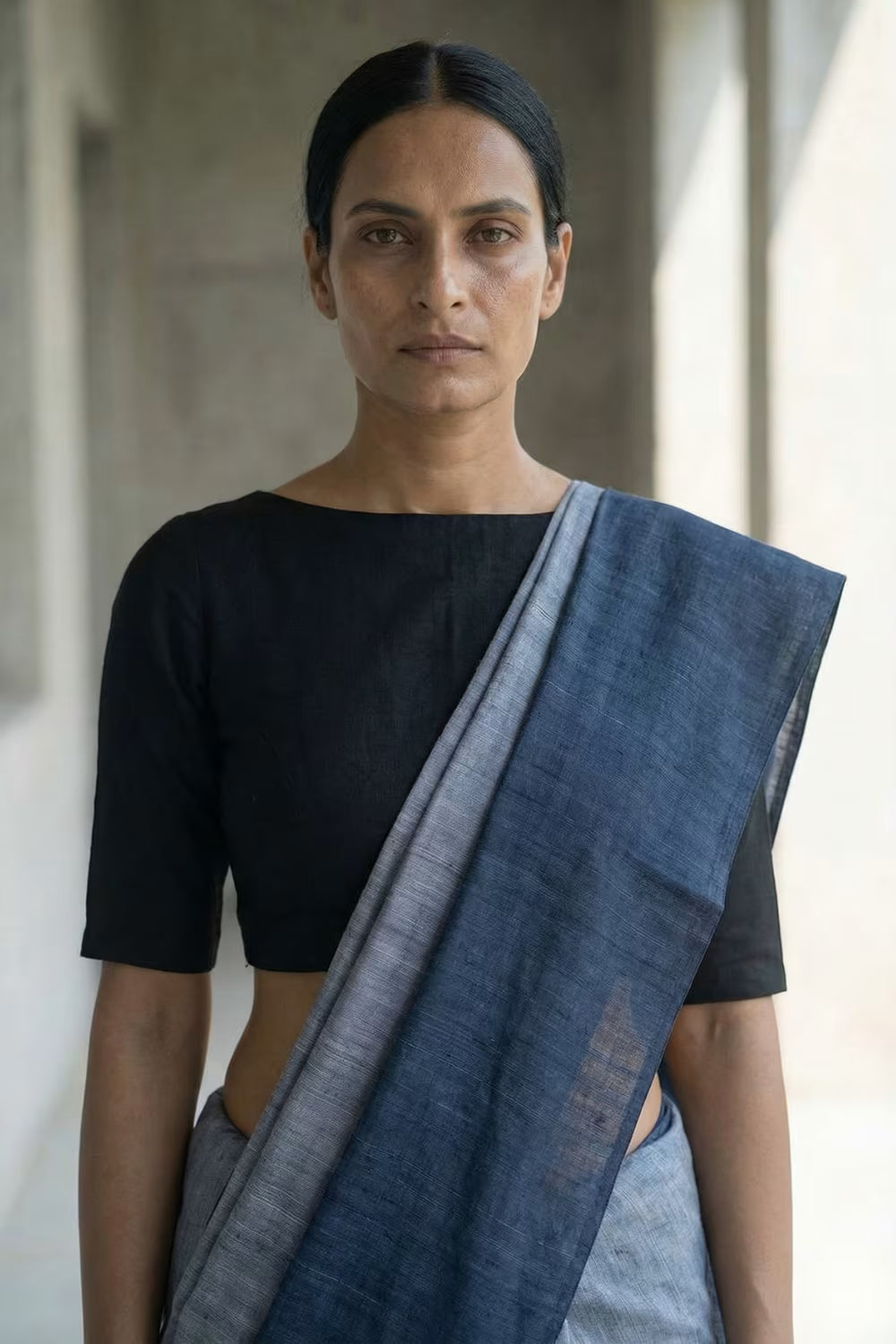 Woman wearing a black top and blue saree against a neutral background