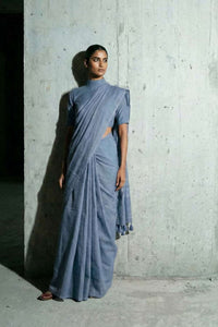 Woman wearing a blue saree against a concrete wall.