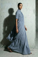 Woman wearing a blue saree against a concrete wall.