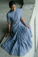 Woman wearing a blue saree sitting on a concrete floor.
