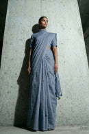 Woman wearing a blue saree standing against a concrete wall.