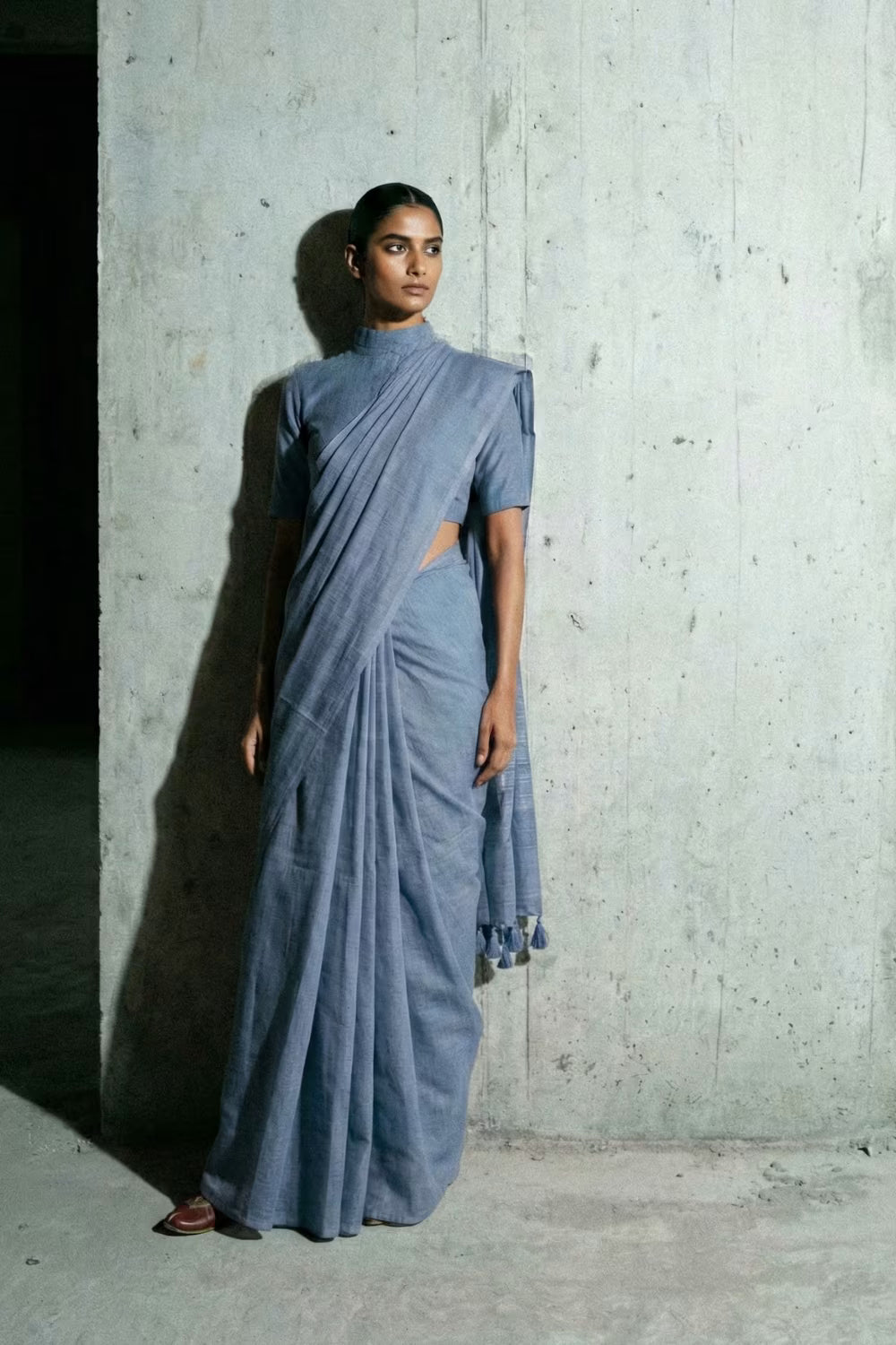 Woman wearing a blue saree against a concrete wall.