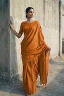 Woman in an orange saree standing against a concrete wall.