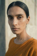 Woman wearing an orange saree against a neutral background